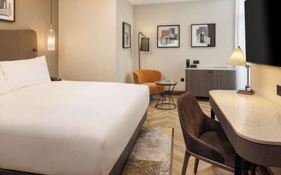 Modern king room with curved desk, leather chair, orange accent seating, and framed wall art