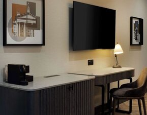 Work desk area with marble countertop, wall-mounted TV, desk lamp, and upholstered chair