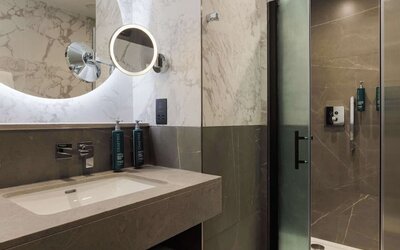 Marble bathroom with illuminated round mirror, modern sink vanity, and glass walk-in shower