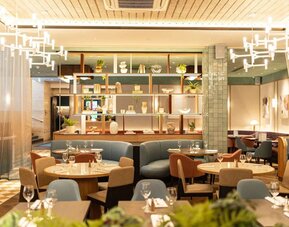 Restaurant dining area with round tables, upholstered seating, decorative shelving, and pendant lights