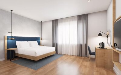 Spacious king room with blue headboard, large curtained window, desk area, and wall-mounted TV
