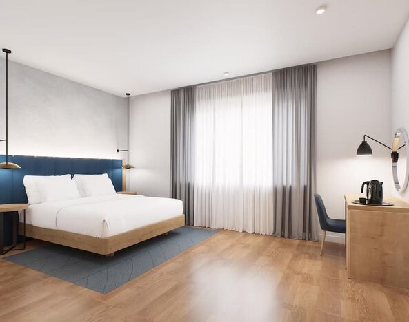 Spacious king room with blue headboard, large curtained window, desk area, and wall-mounted TV