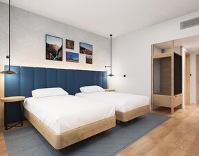Guest room with two beds, blue padded headboard, wood furniture, and framed wall artwork