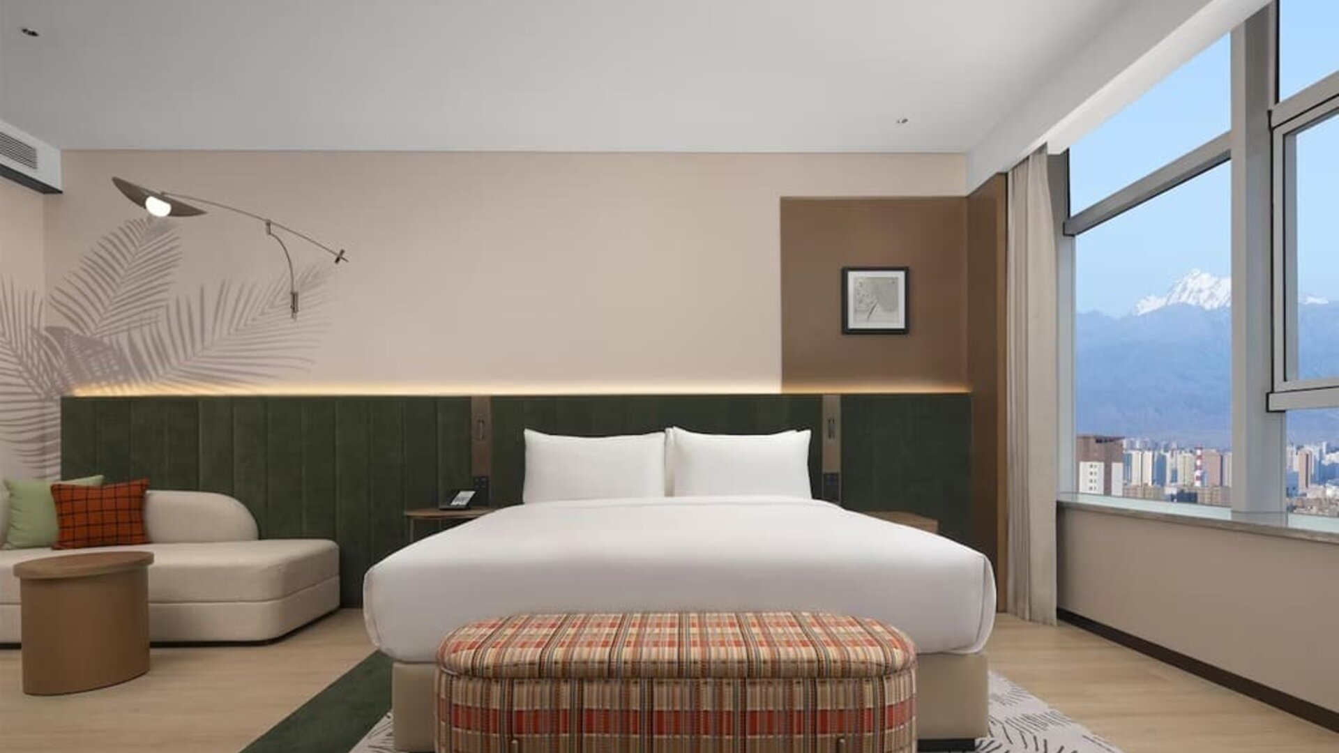 King bedroom with mountain and city views through corner windows, chaise lounge, and patterned bench