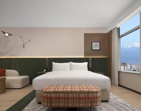 King bedroom with mountain and city views through corner windows, chaise lounge, and patterned bench