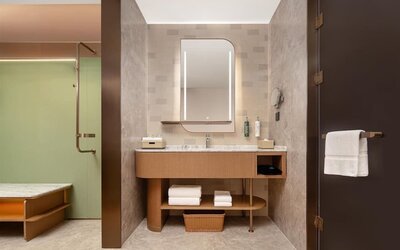 Modern bathroom vanity with illuminated mirror, marble counter, towels, and glass shower entrance