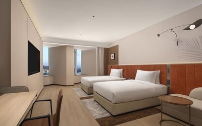 Modern guest room with two double beds, wall-mounted TV, desk area, and corner city windows