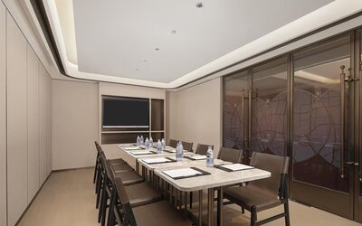 Narrow meeting room with marble conference table, leather chairs, bottled water, and wall-mounted TV
