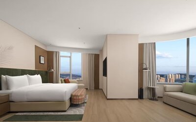 King bedroom with mountain and city views through corner windows, chaise lounge, and patterned bench