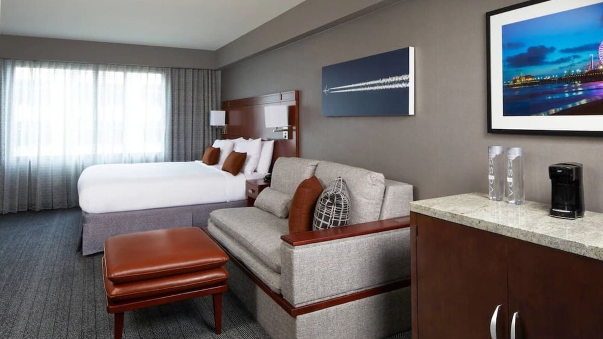 Spacious guest room with king bed, sofa seating area, ottoman, and kitchenette counter at Courtyard By Marriott Los Angeles LAX/Century Boulevard.