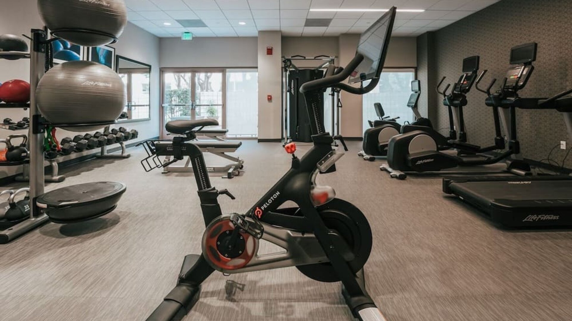Modern hotel gym with Peloton bike, treadmills, elliptical machines, and weight station at Courtyard By Marriott Los Angeles LAX/Century Boulevard.