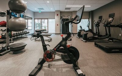 Modern hotel gym with Peloton bike, treadmills, elliptical machines, and weight station at Courtyard By Marriott Los Angeles LAX/Century Boulevard.