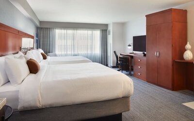 Guest room with two beds, workspace, wardrobe cabinet, and large window at Courtyard By Marriott Los Angeles LAX/Century Boulevard.