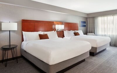 Spacious double queen guest room with modern furnishings, wood headboards, and soft natural lighting at Courtyard By Marriott Los Angeles LAX/Century Boulevard.