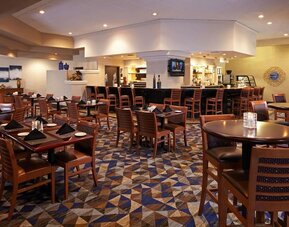 Spacious dining area with restaurant seating, patterned carpet, and central bar area at Embassy Suites By Hilton LAX Airport North.