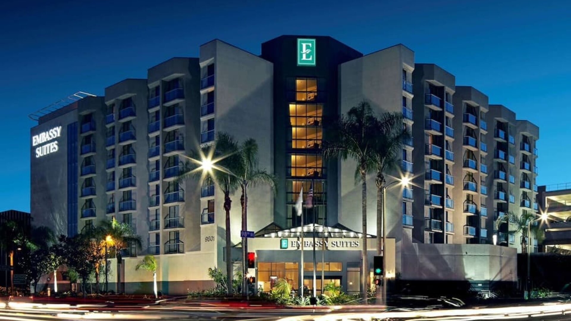 Evening exterior view of the hotel building with lit windows and palm-lined street at Embassy Suites By Hilton LAX Airport North.