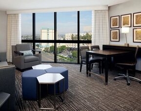 Spacious suite living area with city views, dining table, lounge seating, and floor-to-ceiling windows at Embassy Suites By Hilton LAX Airport North.