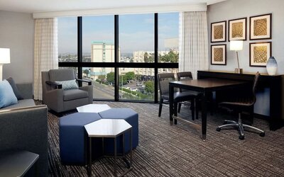 Spacious suite living area with city views, dining table, lounge seating, and floor-to-ceiling windows at Embassy Suites By Hilton LAX Airport North.