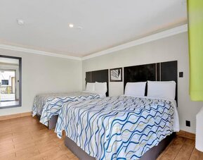 Guest room with two double beds, tiled flooring, modern lighting, and wall-mounted TV at Mid City Inn - Los Angeles.