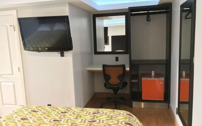 In-room workspace with desk, chair, mini fridge, wall-mounted TV, and open closet area at Mid City Inn - Los Angeles.