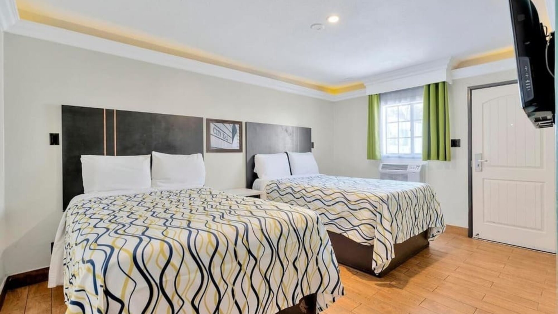 Spacious double-bed guest room with wood-style flooring, modern décor, and bright accent curtains at Mid City Inn - Los Angeles.