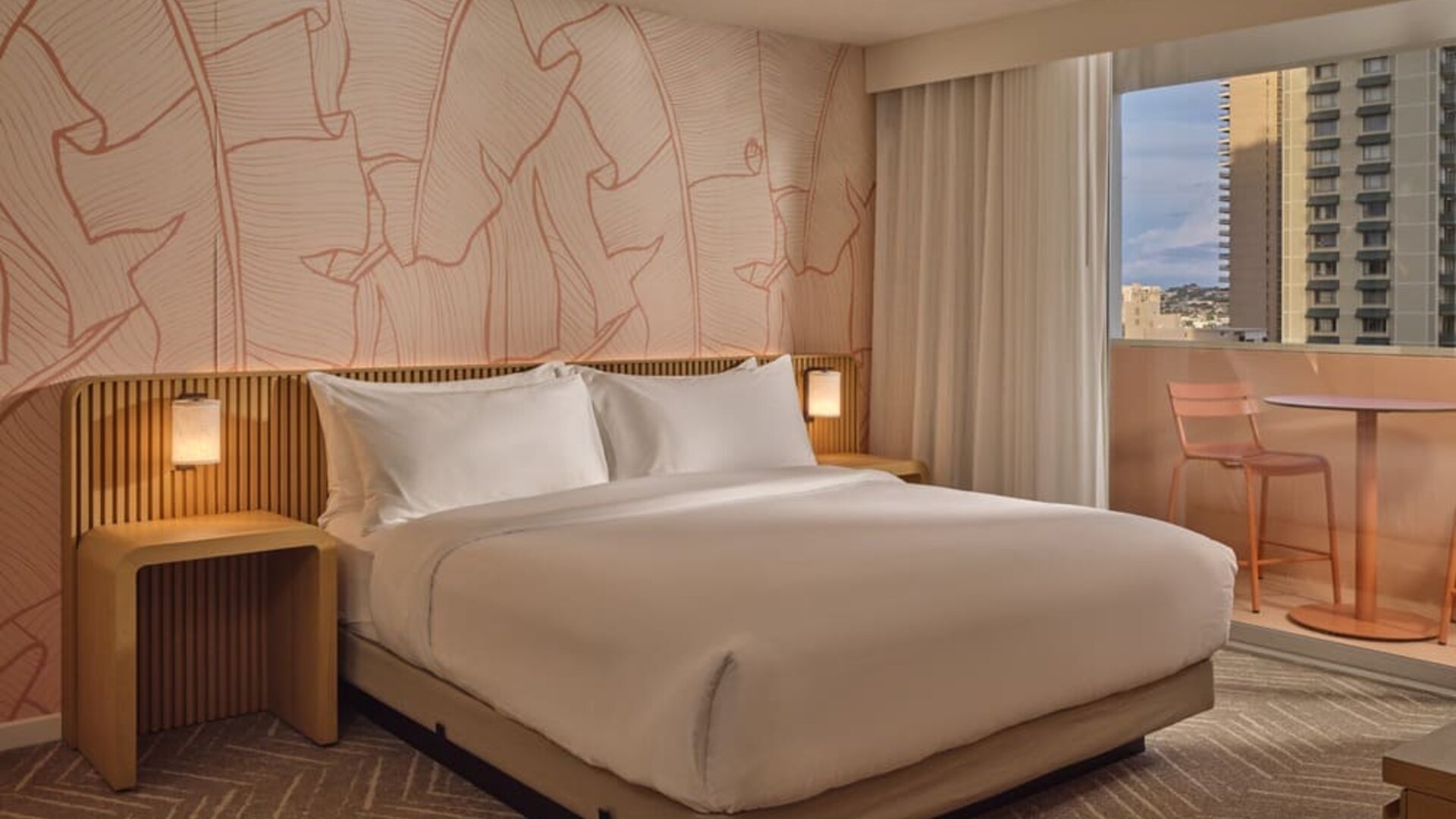 Guest room with king-size bed, modern wood accents, soft ambient lighting, and private balcony seating overlooking Waikiki at The Ambassador Hotel Of Waikiki