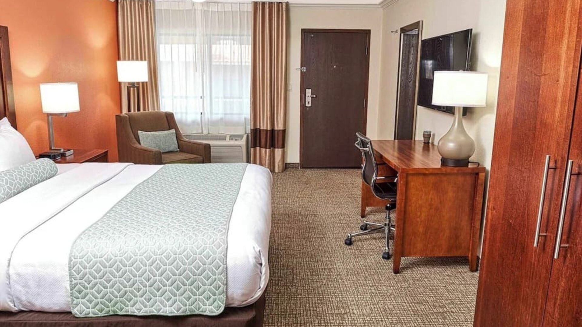 King guest room with work desk, armchair, large window, and warm orange accent wall at The Hills Inn Eagle Rock.
