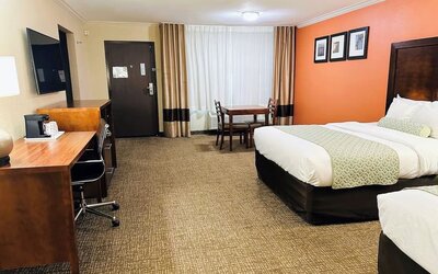 Spacious guest room with two beds, work desk, dining table, and orange accent wall at The Hills Inn Eagle Rock.