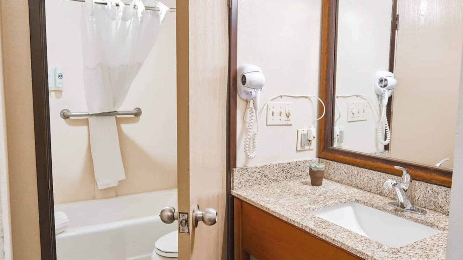 Bathroom with granite vanity, large mirror, bathtub shower combo, and mounted hair dryer at The Hills Inn Eagle Rock.