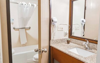 Bathroom with granite vanity, large mirror, bathtub shower combo, and mounted hair dryer at The Hills Inn Eagle Rock.