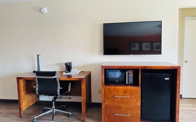 Work area with desk chair, flat-screen TV, microwave, mini fridge, and wood flooring at The Hills Inn Eagle Rock.