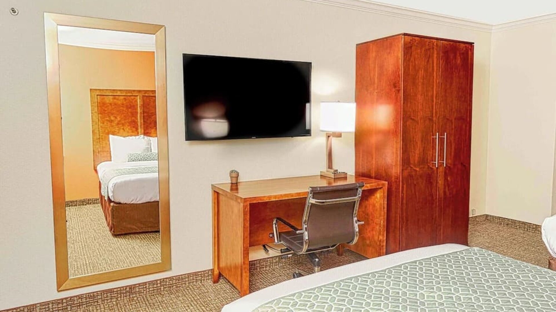 Guest room with mounted TV, wooden wardrobe, desk workspace, and full-length mirror at The Hills Inn Eagle Rock.