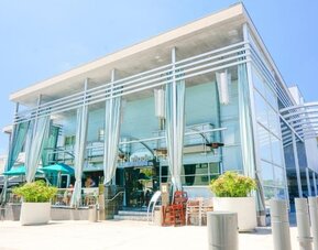 Modern glass-front hotel entrance with tall draped curtains and outdoor seating at Shade Hotel Manhattan Beach.