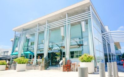 Modern glass-front hotel entrance with tall draped curtains and outdoor seating at Shade Hotel Manhattan Beach.