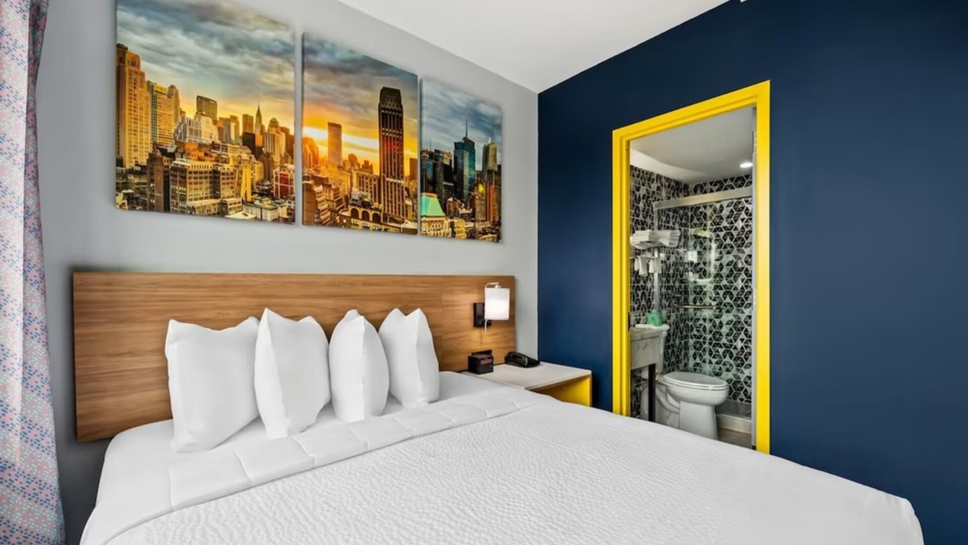 Queen bedroom with bold blue accent wall, skyline artwork, and patterned bathroom tiles at Days Inn Chinatown NYC.