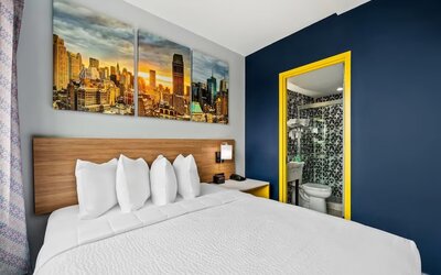 Queen bedroom with bold blue accent wall, skyline artwork, and patterned bathroom tiles at Days Inn Chinatown NYC.