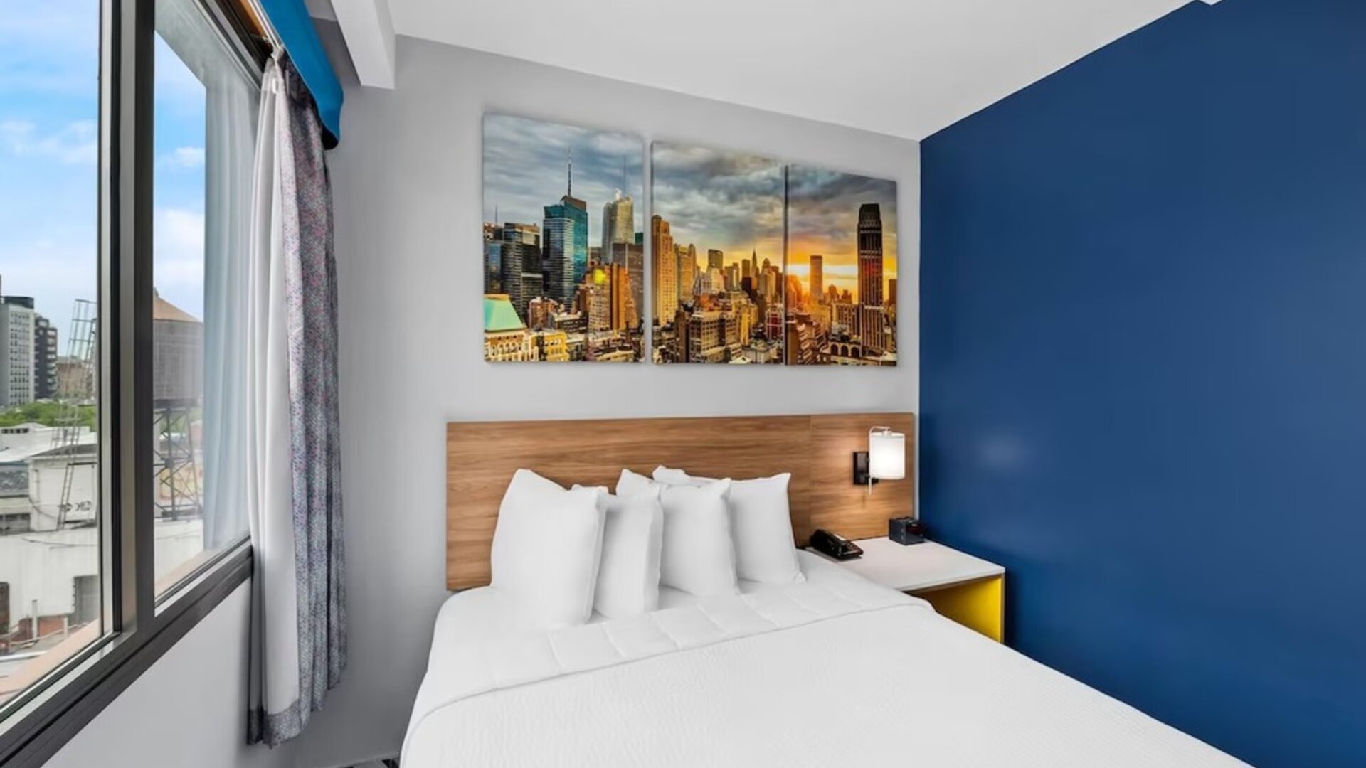 Bright guest room with queen bed, skyline canvas art, and corner city-view windows at Days Inn Chinatown NYC.