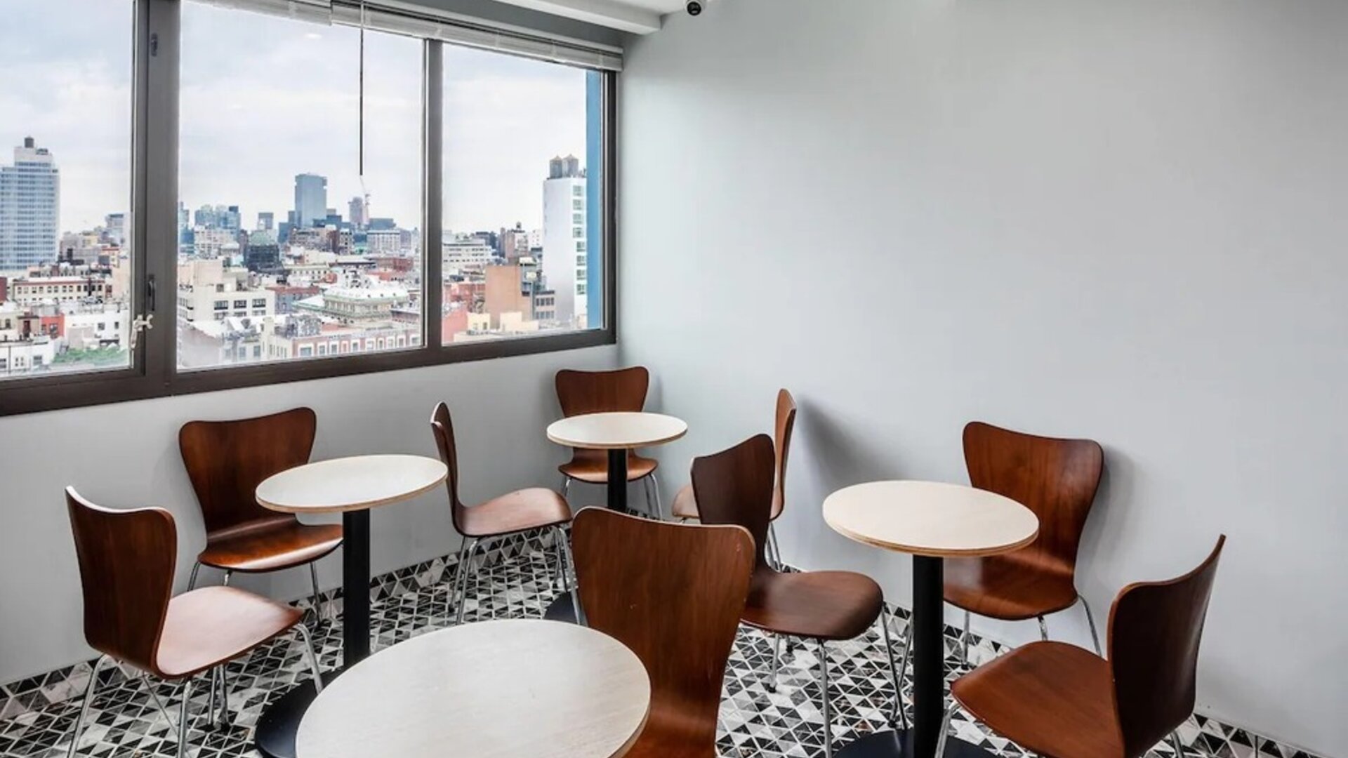 Small dining area with round tables, wooden chairs, and panoramic city skyline views at Days Inn Chinatown NYC.