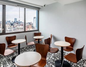 Small dining area with round tables, wooden chairs, and panoramic city skyline views at Days Inn Chinatown NYC.