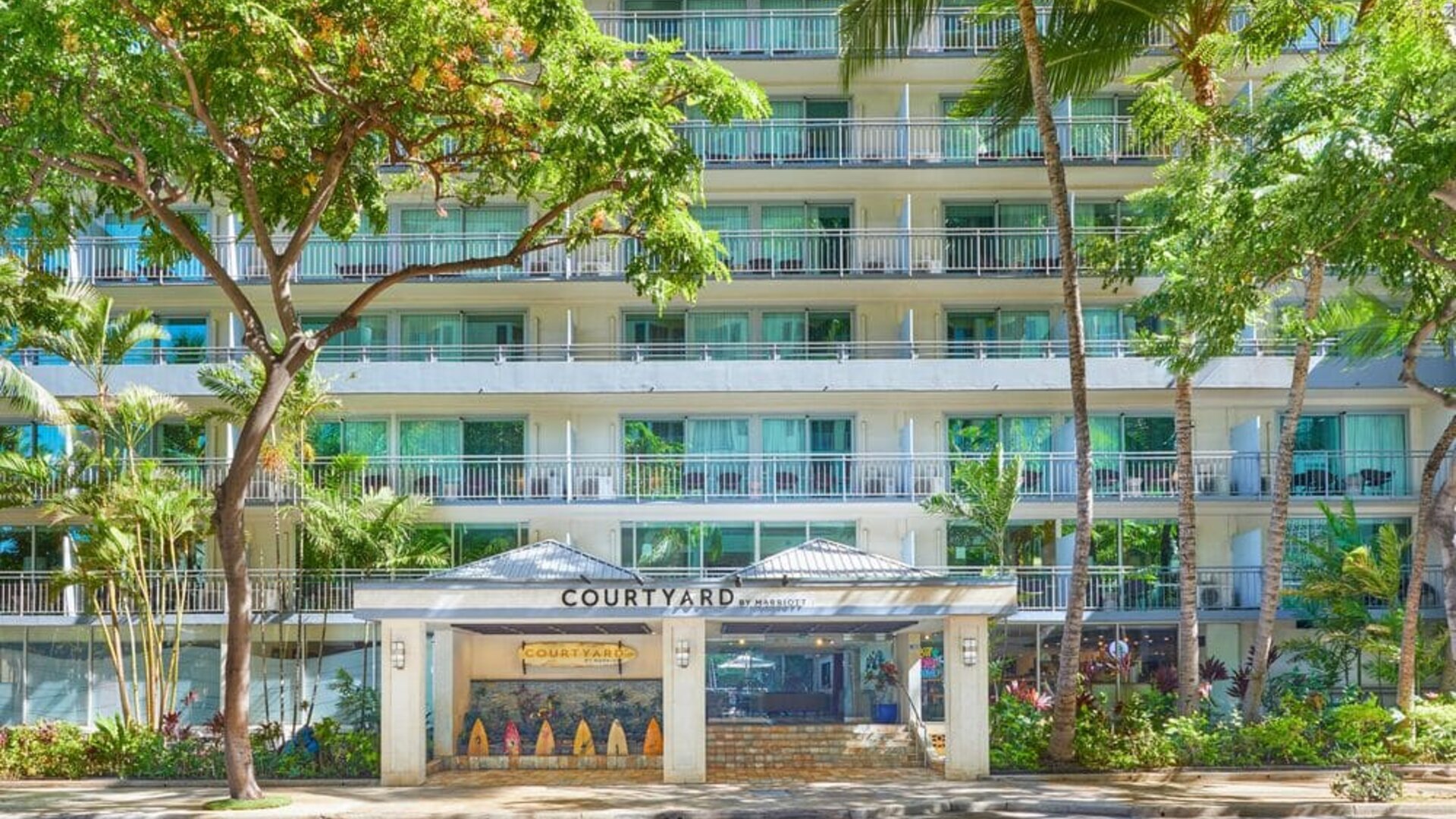 Front entrance of Courtyard Waikiki Beach surrounded by tropical landscaping.