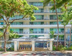 Front entrance of Courtyard Waikiki Beach surrounded by tropical landscaping.