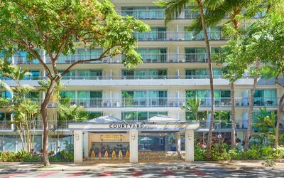 Front entrance of Courtyard Waikiki Beach surrounded by tropical landscaping.