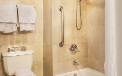 Accessible bathroom with bathtub, grab bars, and modern fixtures at Courtyard By Marriott New York JFK Airport.