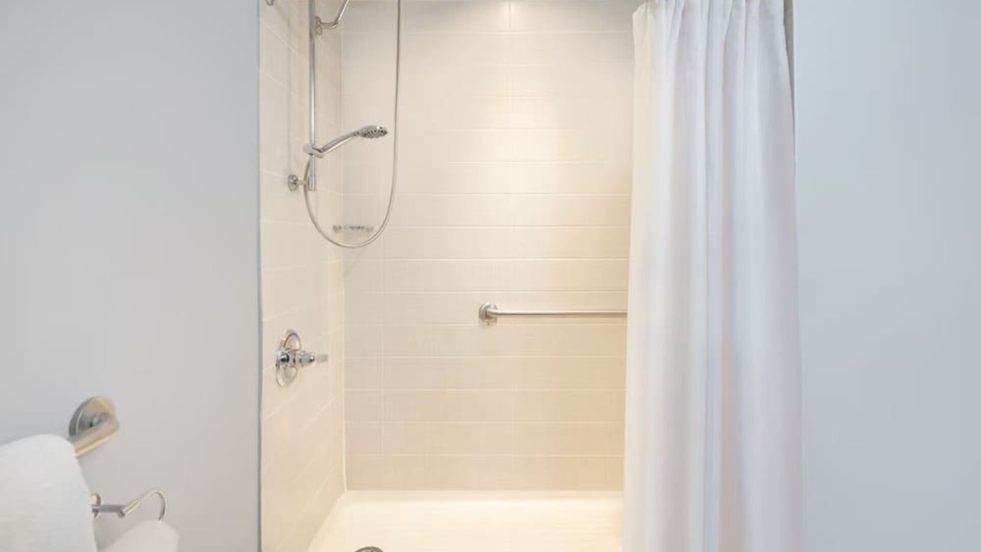 Accessible walk-in shower bathroom with safety handrails at Courtyard By Marriott New York JFK Airport.