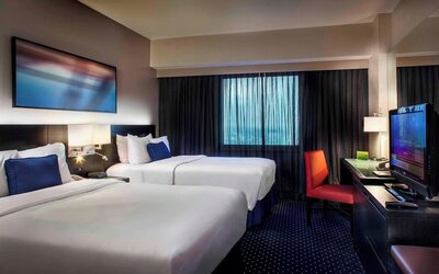 Spacious guest room with two beds, workspace, and city-style décor at Courtyard By Marriott New York JFK Airport.