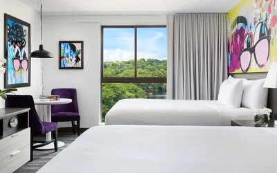 Bright double queen guest room with colorful wall art and large windows at Hotel Studio Allston.