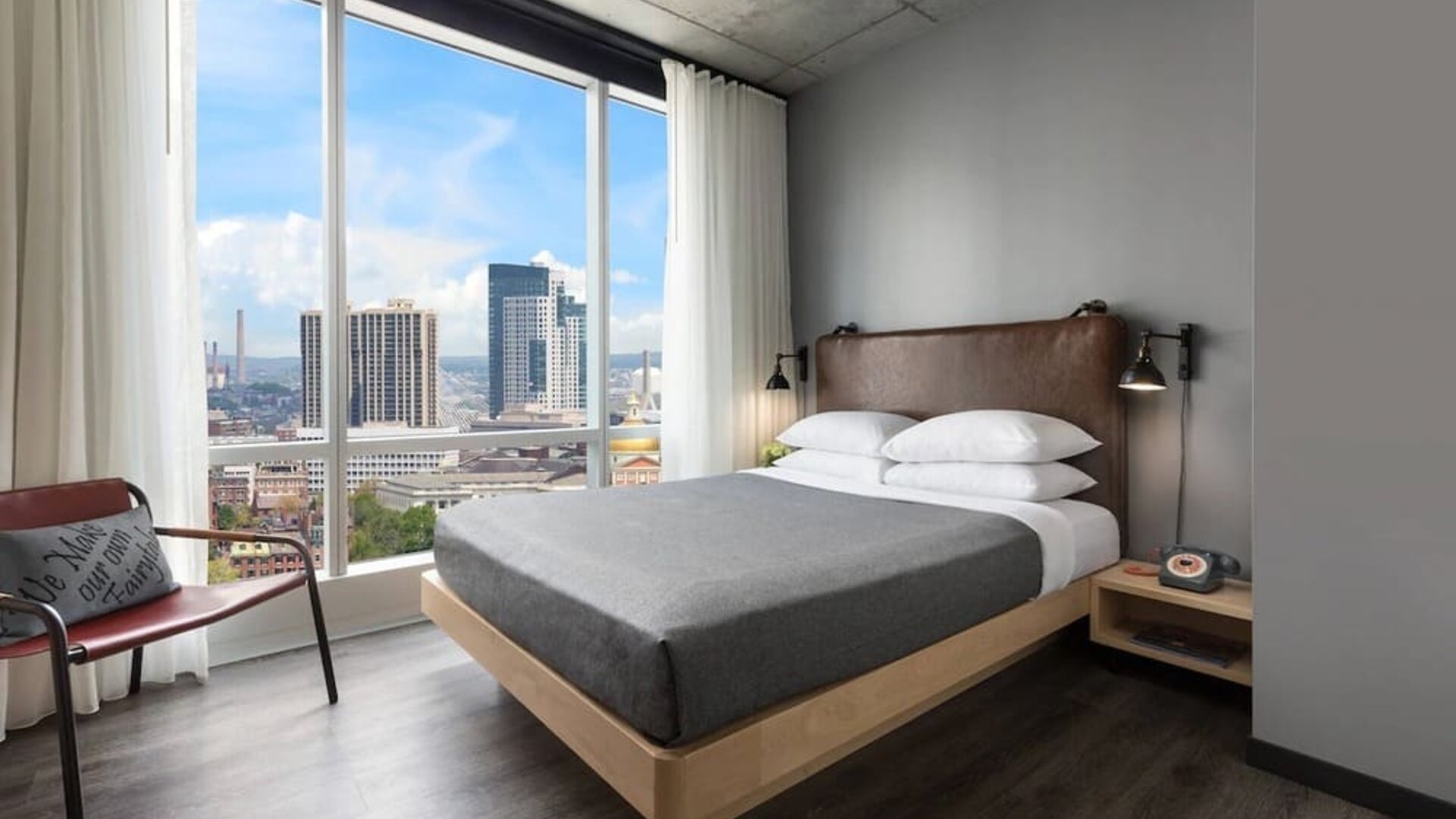 Guest room with platform bed and floor-to-ceiling windows overlooking the Boston skyline at Moxy Boston Downtown.
