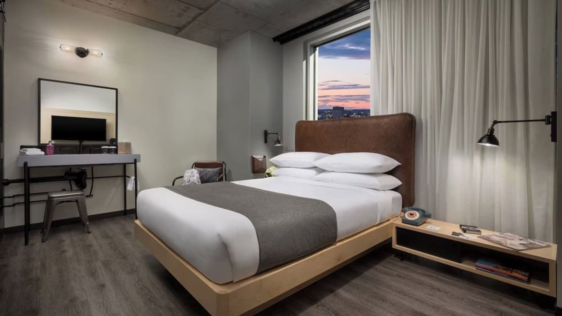 Modern guest room with platform bed, workspace, and large window views at Moxy Boston Downtown.
