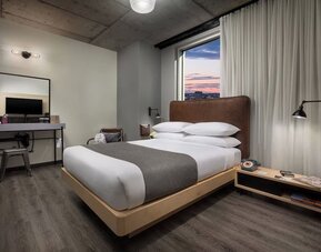 Modern guest room with platform bed, workspace, and large window views at Moxy Boston Downtown.