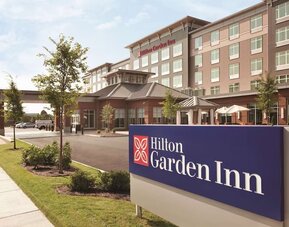 Daytime exterior of Hilton Garden Inn Boston Logan Airport with branded roadside signage and landscaped entrance.